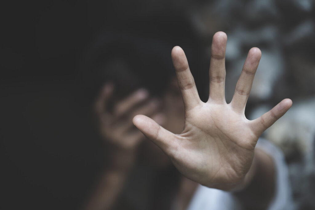A woman holds up her hand to defend herself against an attacker