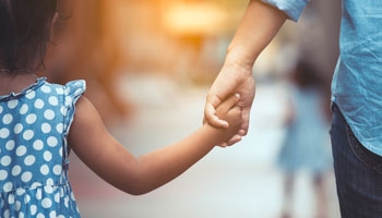 young kid and young adult holding hands and walking down the street