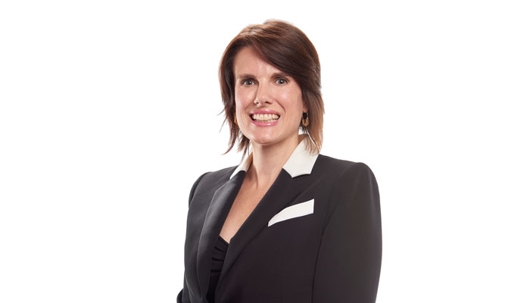 A professional headshot features a woman with dark hair, smiling and wearing a black blazer with white trim.