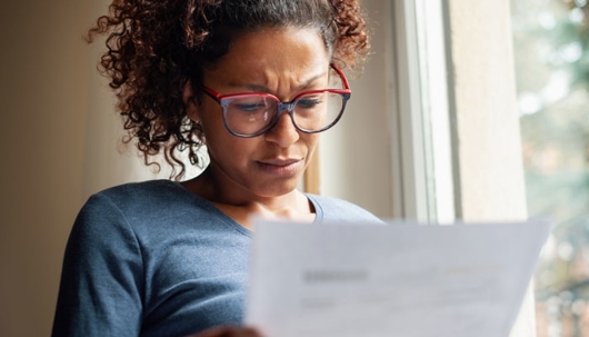 A woman in glasses holds a document and looks concerned.