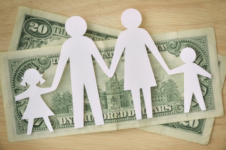A paper cutout of a family stands on two twenty-dollar bills, symbolizing financial aspects of child support.