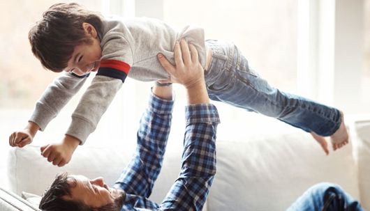A father lies on his back holding his son in the air.