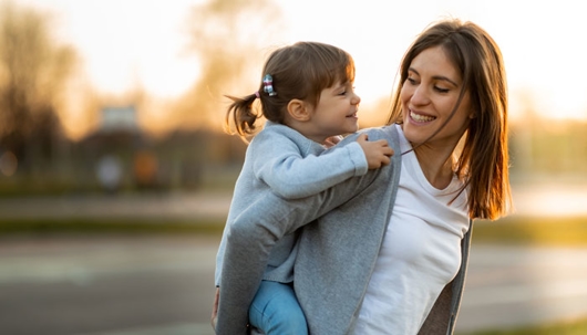 Smiling mother carrying her young daughter on her back outside.