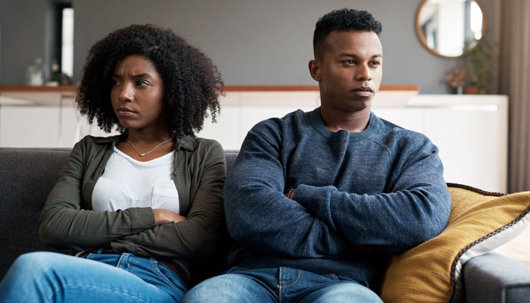 a distressed young couple sit on the couch together