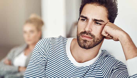A man in a striped shirt looks pensive while a woman with her arms crossed