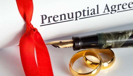 a closeup shot of a prenuptial agreement document, a pen, and 2 wedding rings