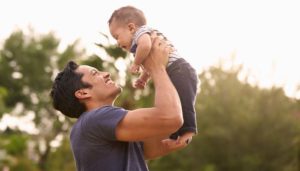 father holds his young son in the air and they smile at each other