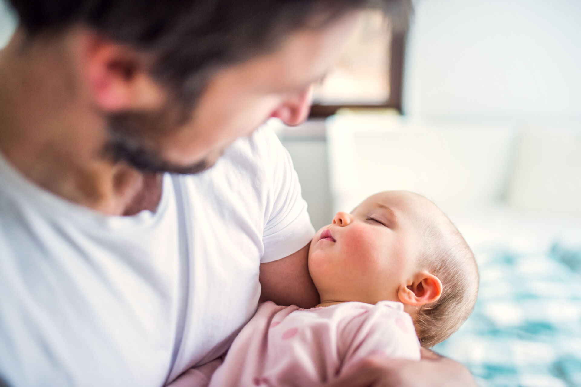 Father holding a sleeping toddler girl at home.