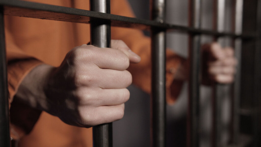 Man in Jail - Hands on Cell Bars of Prison